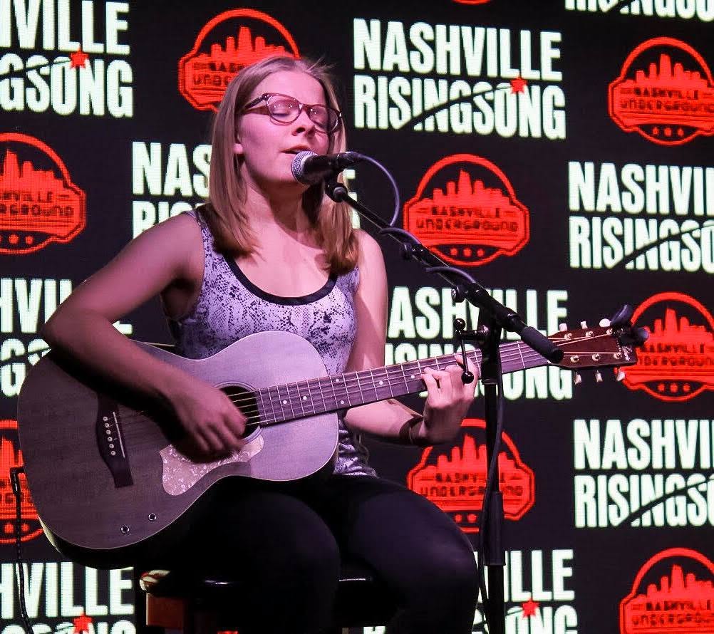 A songwriter singing and playing acoustic guitar at Nashville Rising Song