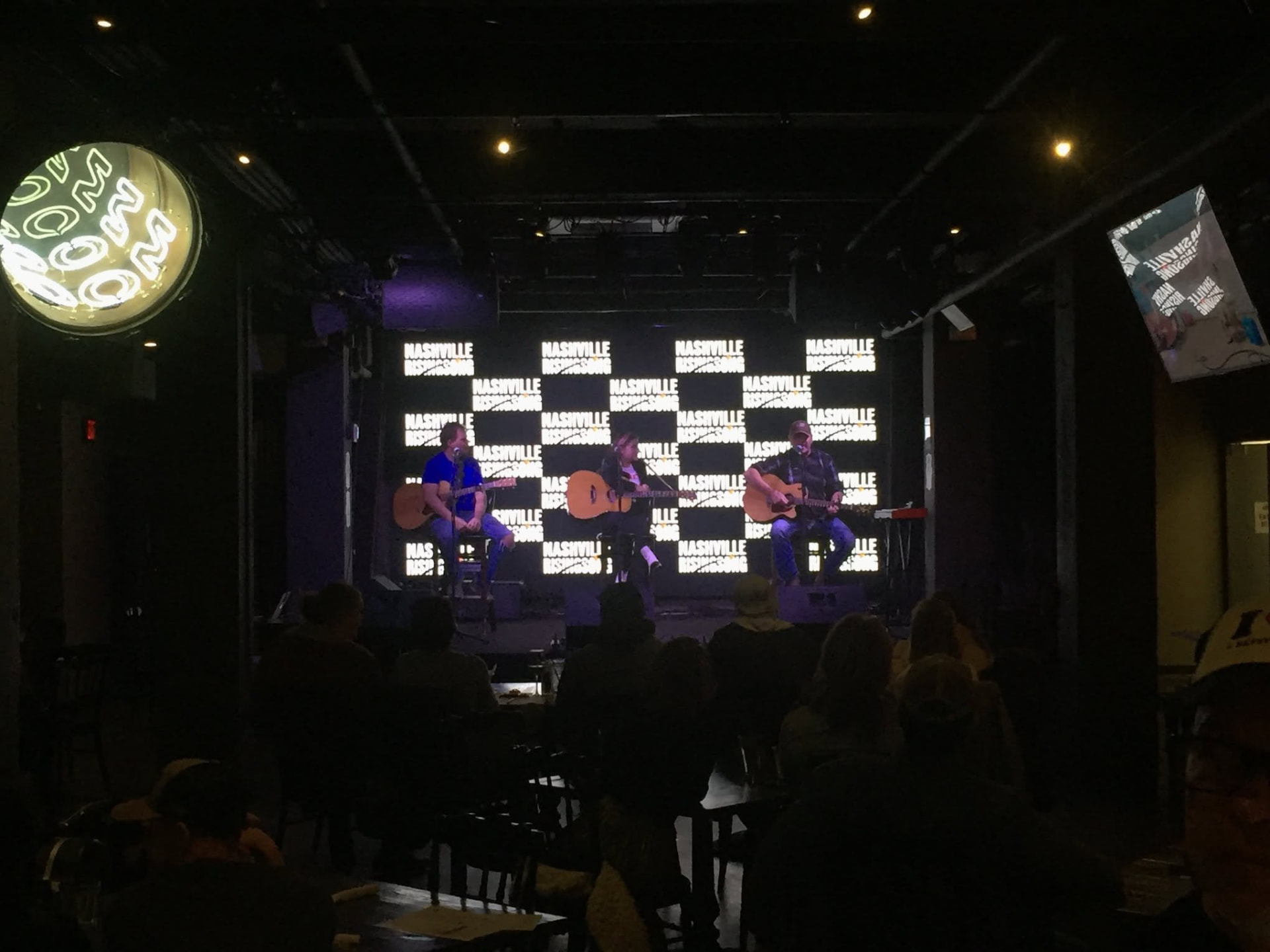 An audience watching three songwriters perform on stage