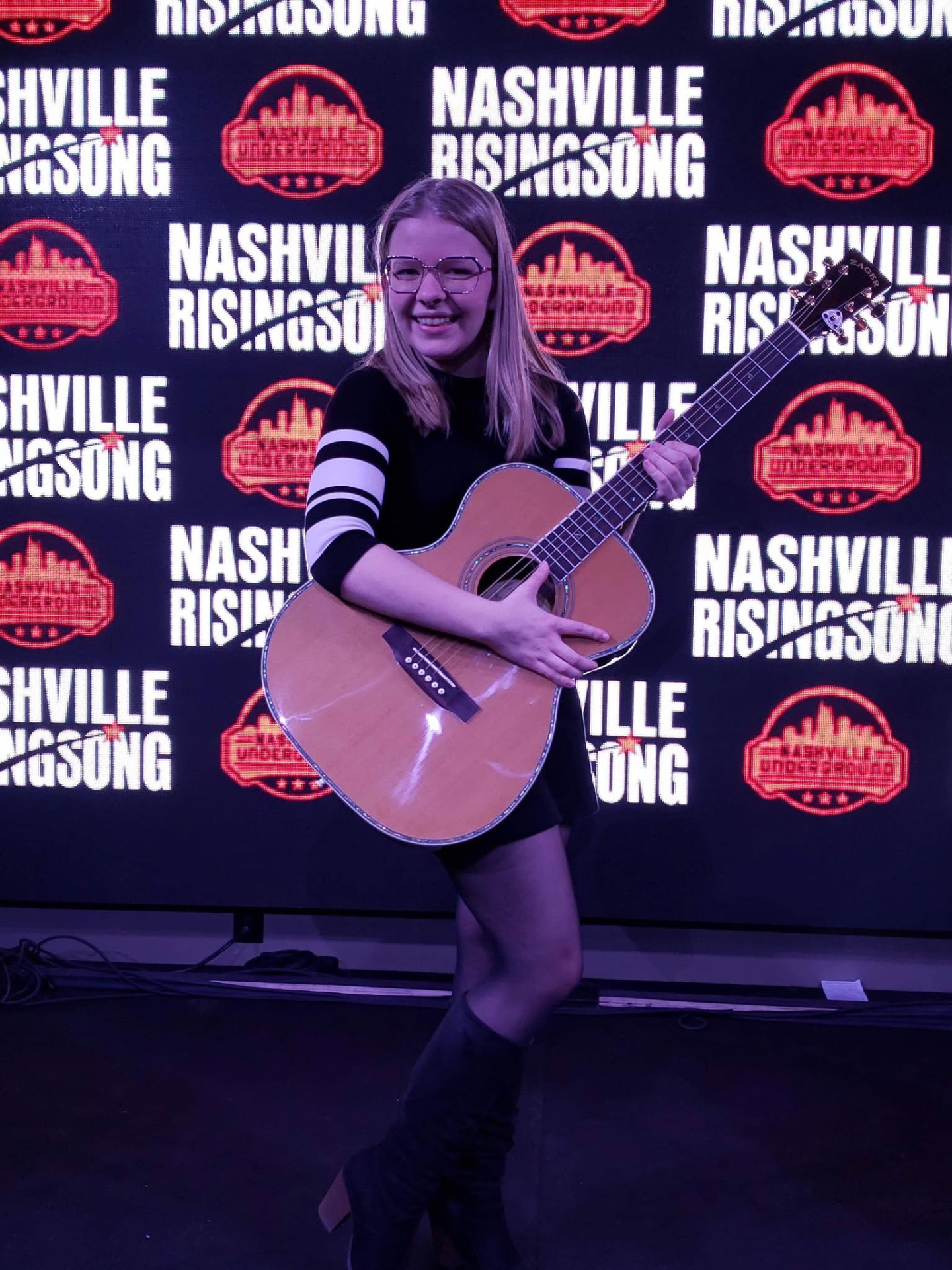 A songwriter with her guitar in front of the Nashville Rising Song stage backdrop